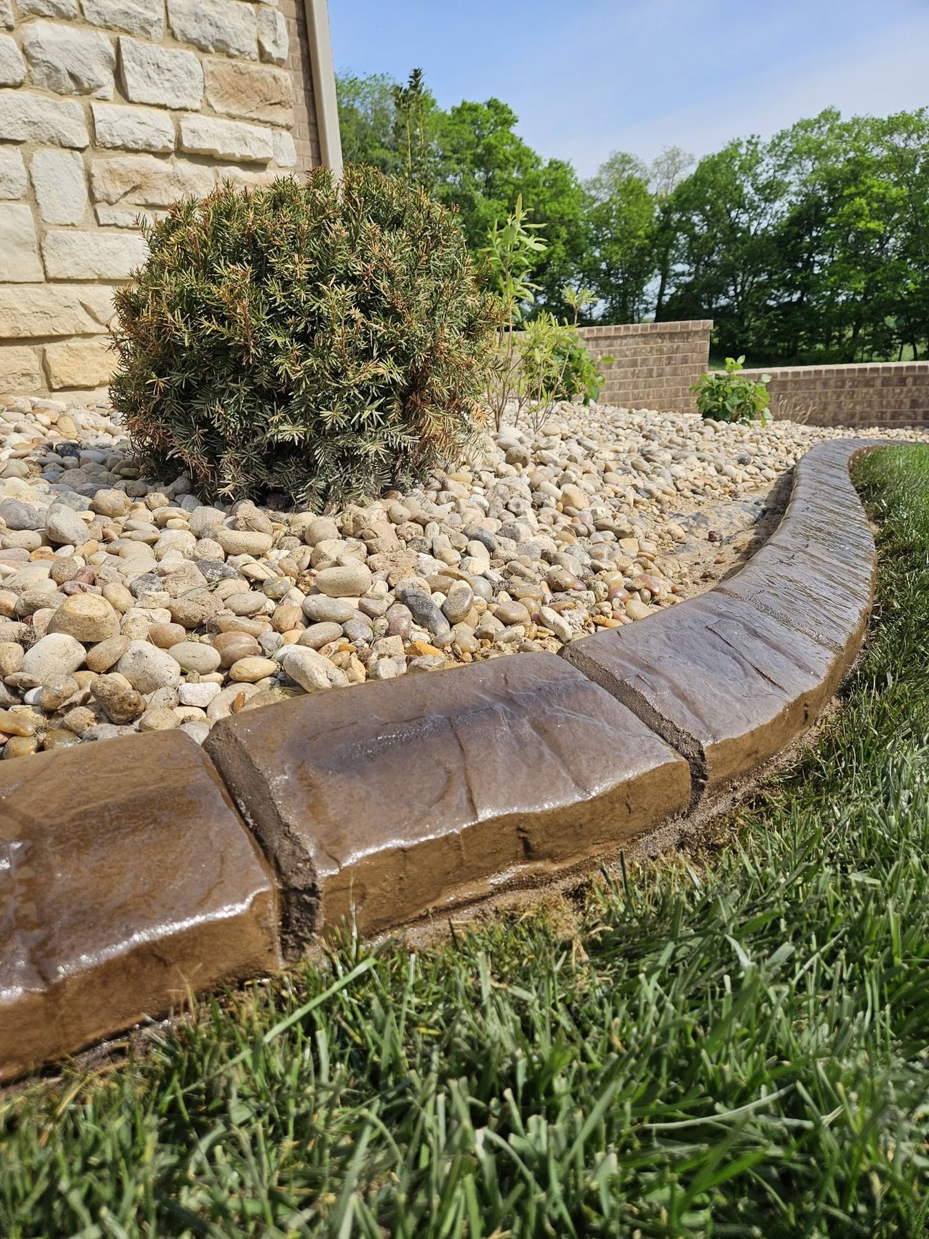 Close-up of warm brown textured concrete curbing beside a river rock planting bed
